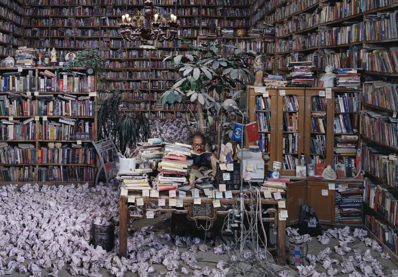 Une homme lit un livre dans une pièce remplie d'étagères