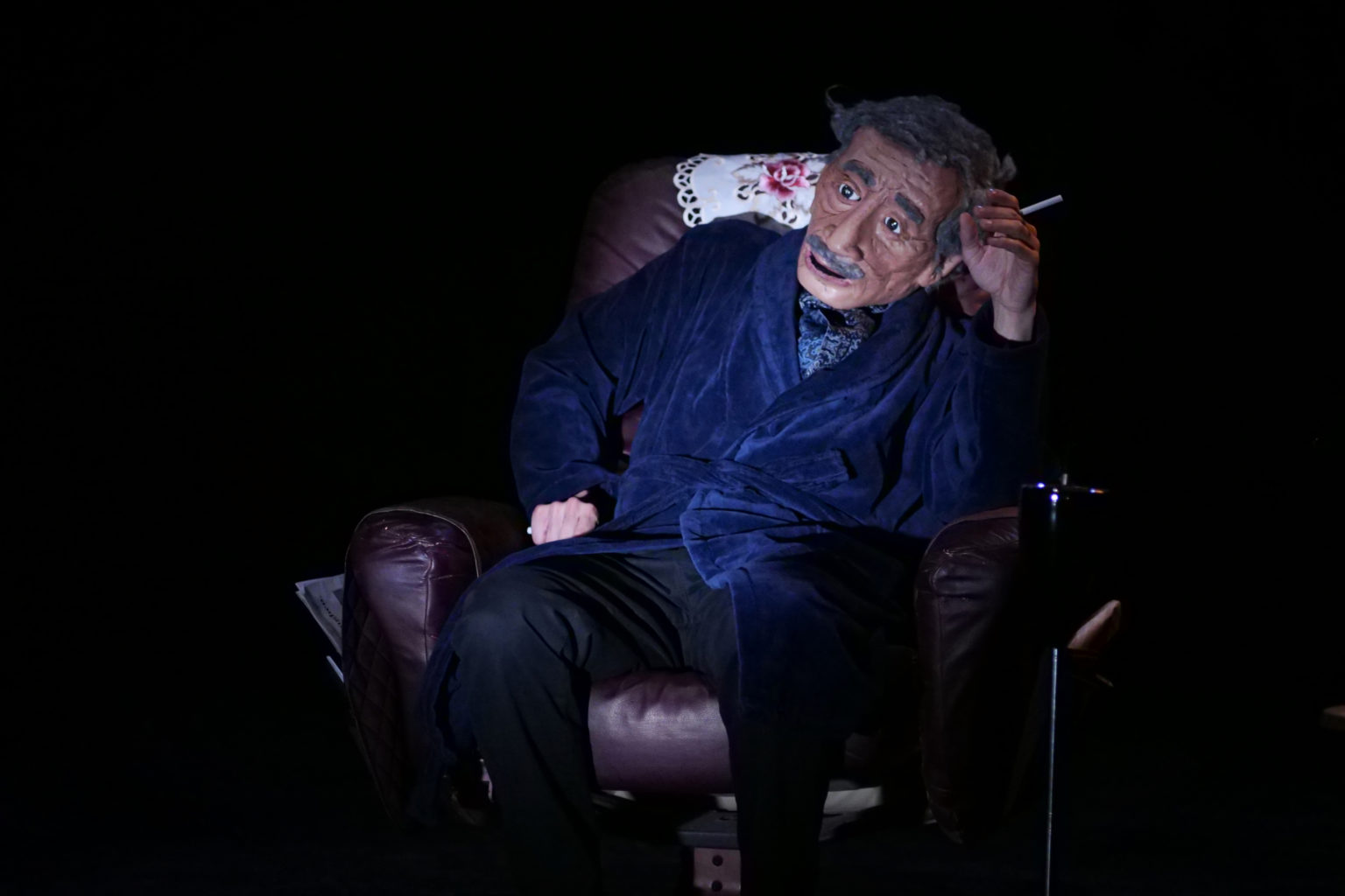 Photo du spectacle "Parti en fumée" où l'on voit la marionnette représentant le père d'Othmane Moumen. Il est assis dans un fauteuil et il fume.
