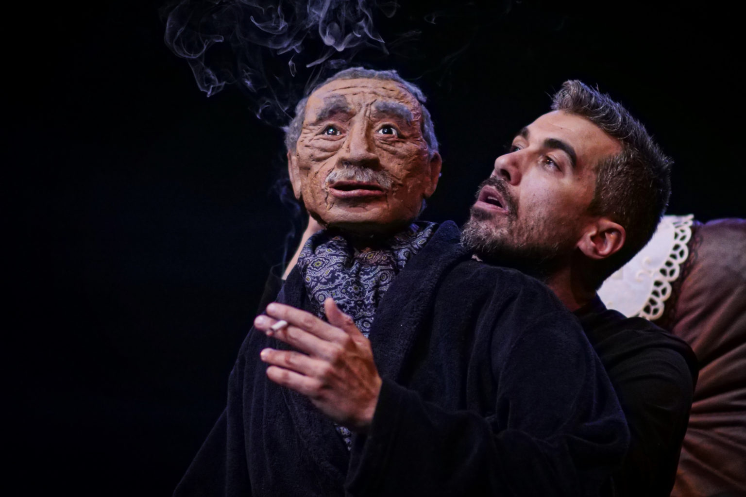 Photo du spectacle "Parti en fumée" où l'on voit le comédien Othmane Moumen avec une marionnette représentant son père. Il fume.