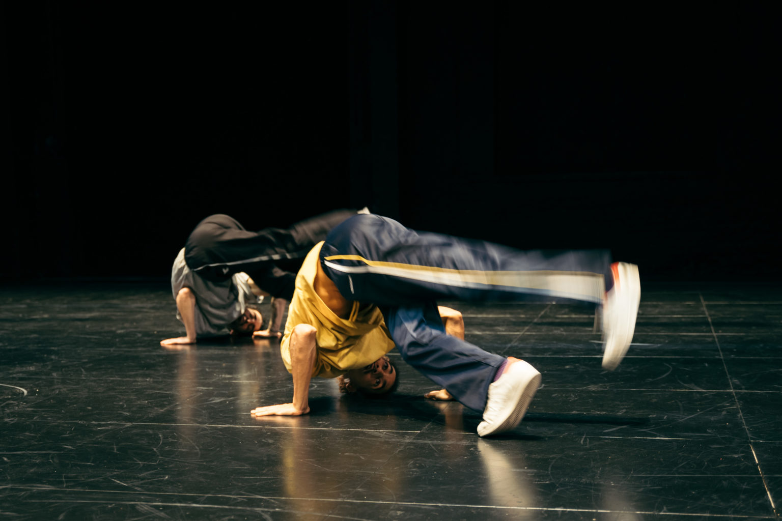 Deux danseurs effectuent un mouvement de breakdance, la tête au sol.