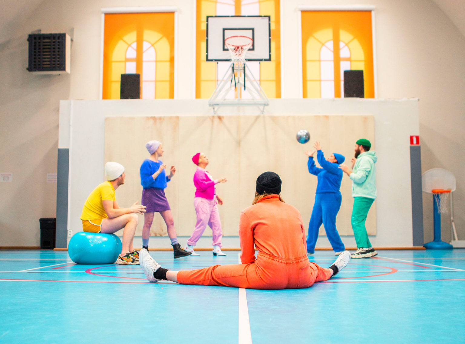 On voit les six acteur·rices de la pièce qui jouent au ballon dans une salle de gymnastique (ancienne église réaffectée en salle de gym)