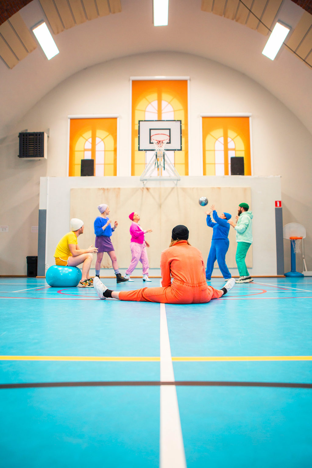 On voit les six acteur·rices de la pièce qui jouent au ballon dans une salle de gymnastique (ancienne église réaffectée en salle de gym)