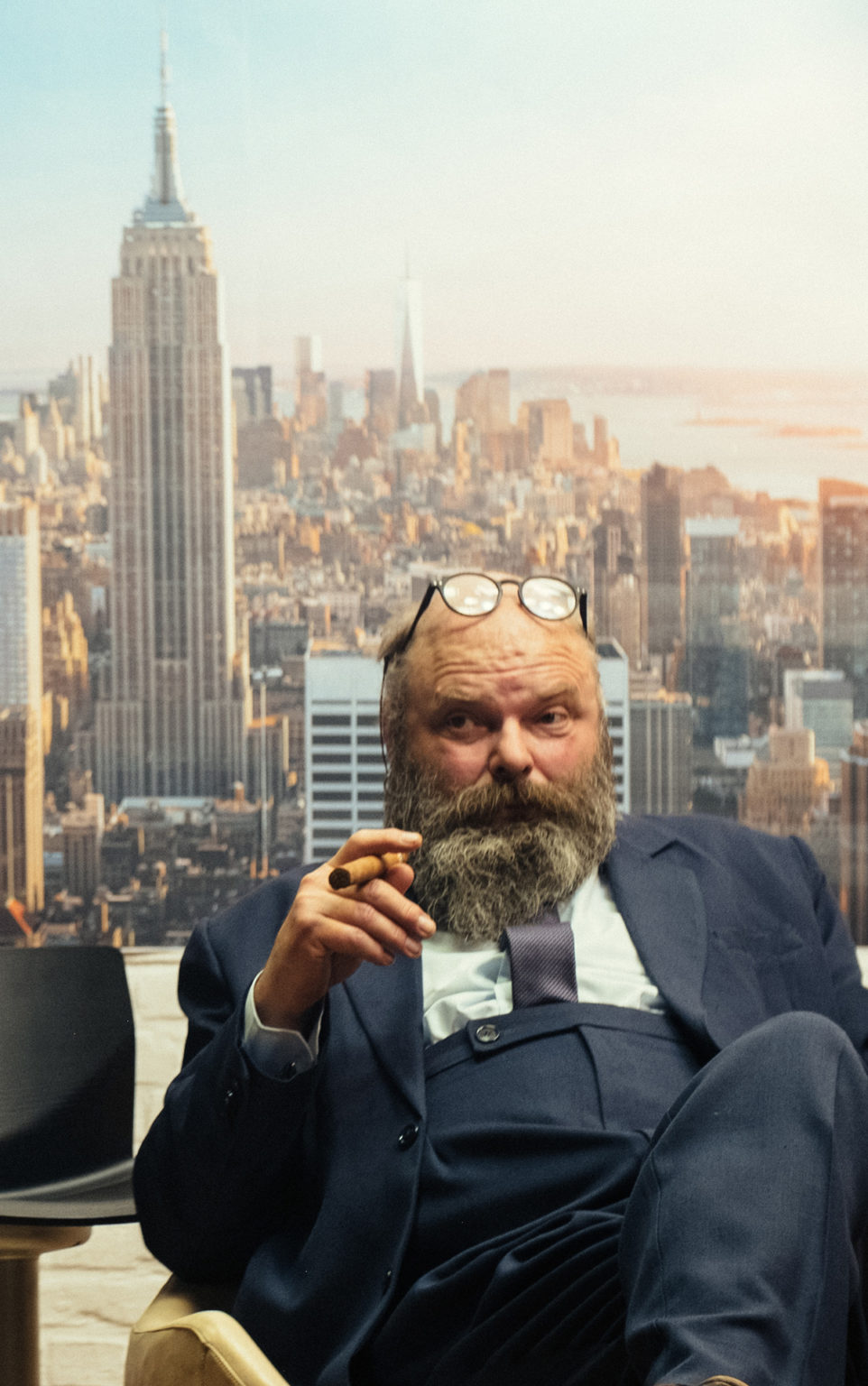 Les acteurs Bert Haelvoet et Damiaan De Schrijver discutent, cigares à la main. Derrière eux, une photo de New York où l'on voit l'Empire State Building.