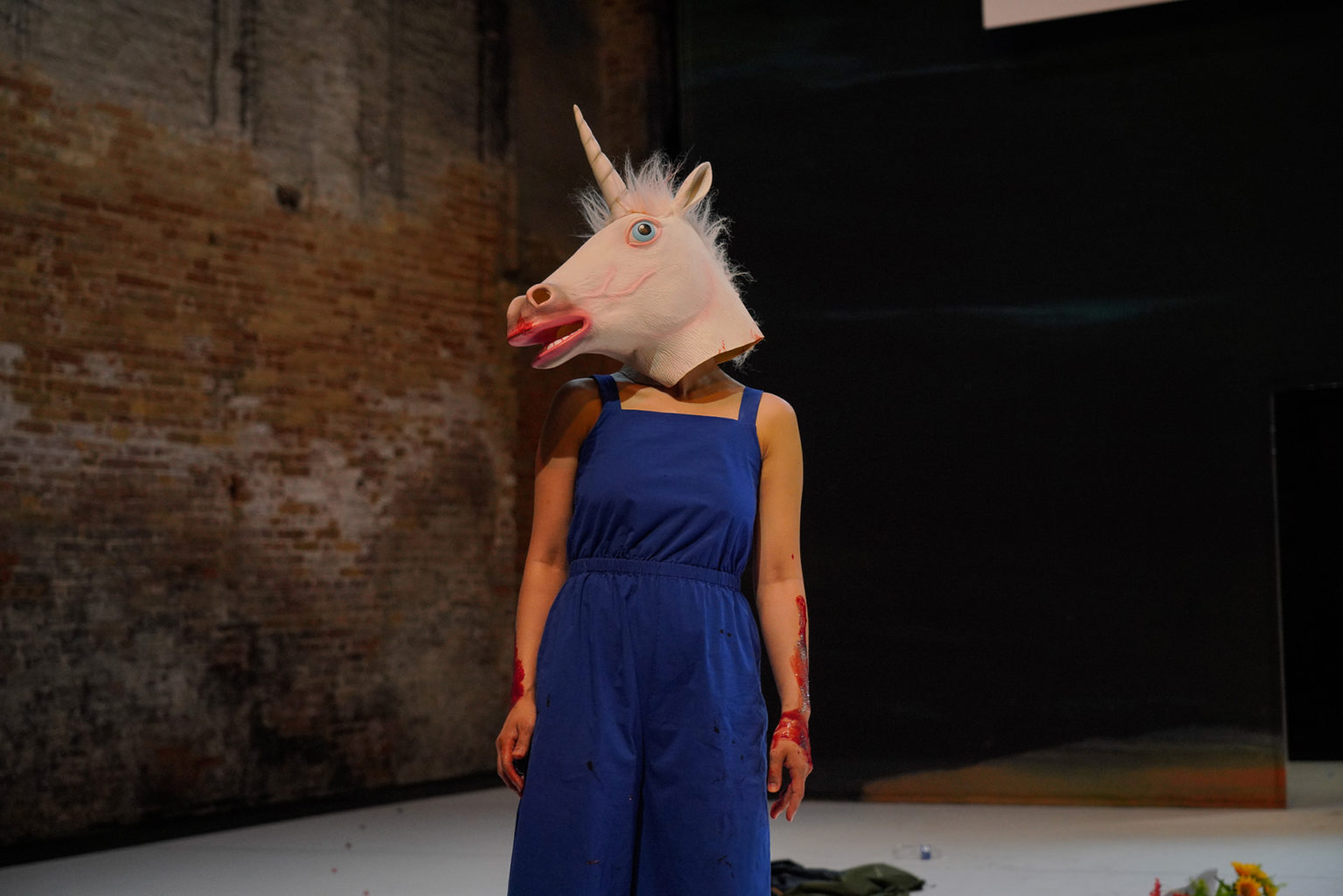 Une actrice, habillée avec une combi bleue, porte un tête de licorne sur la tête.