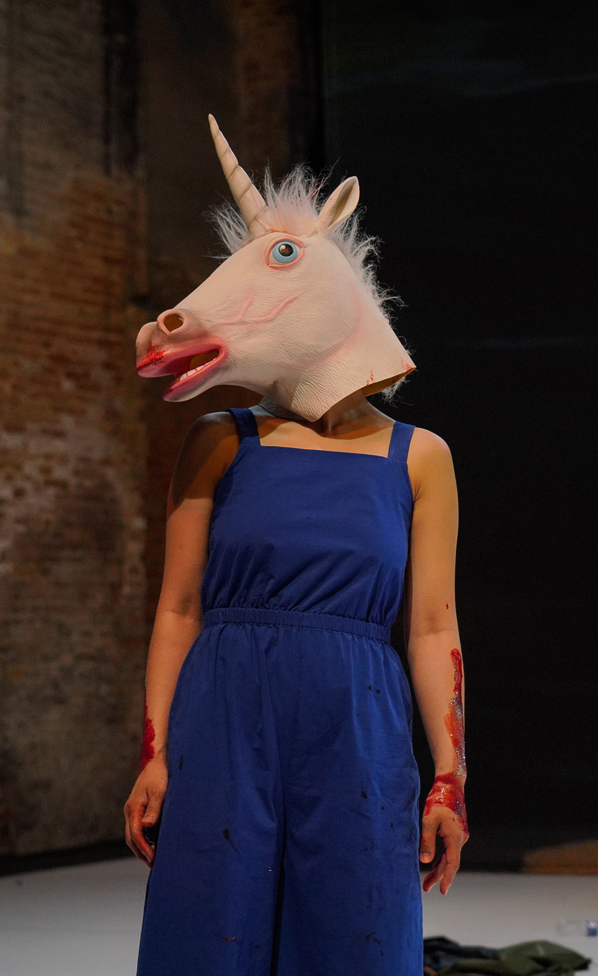 Une actrice, habillée avec une combi bleue, porte un tête de licorne sur la tête.