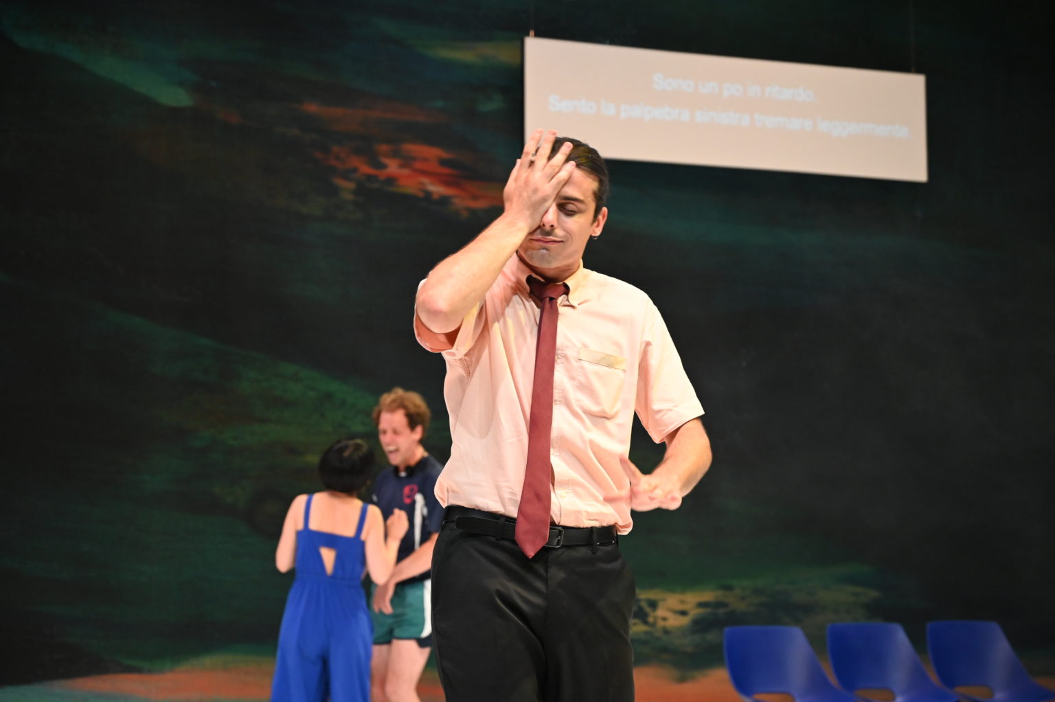 Photo du spectacle "Una foresta" où l'on voit un comédien en avant-plan qui se prend le visage avec sa main, et en arrière-plan deux comédiens discutent