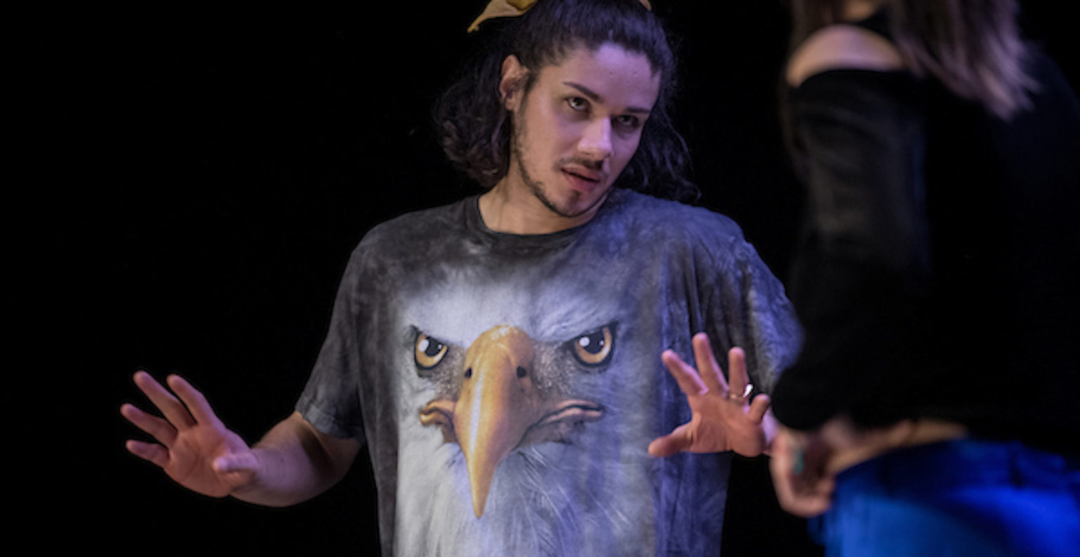 On voit un acteur de la pièce Orphans tendre les bras, les mains ouvertes. Il porte un t-shirt avec une tête d'aigle.