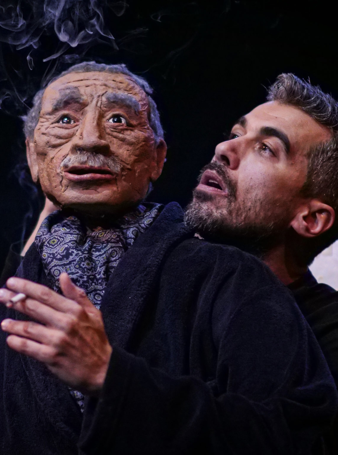 Photo du spectacle "Parti en fumée" où l'on voit le comédien Othmane Moumen avec une marionnette représentant son père. Il fume.