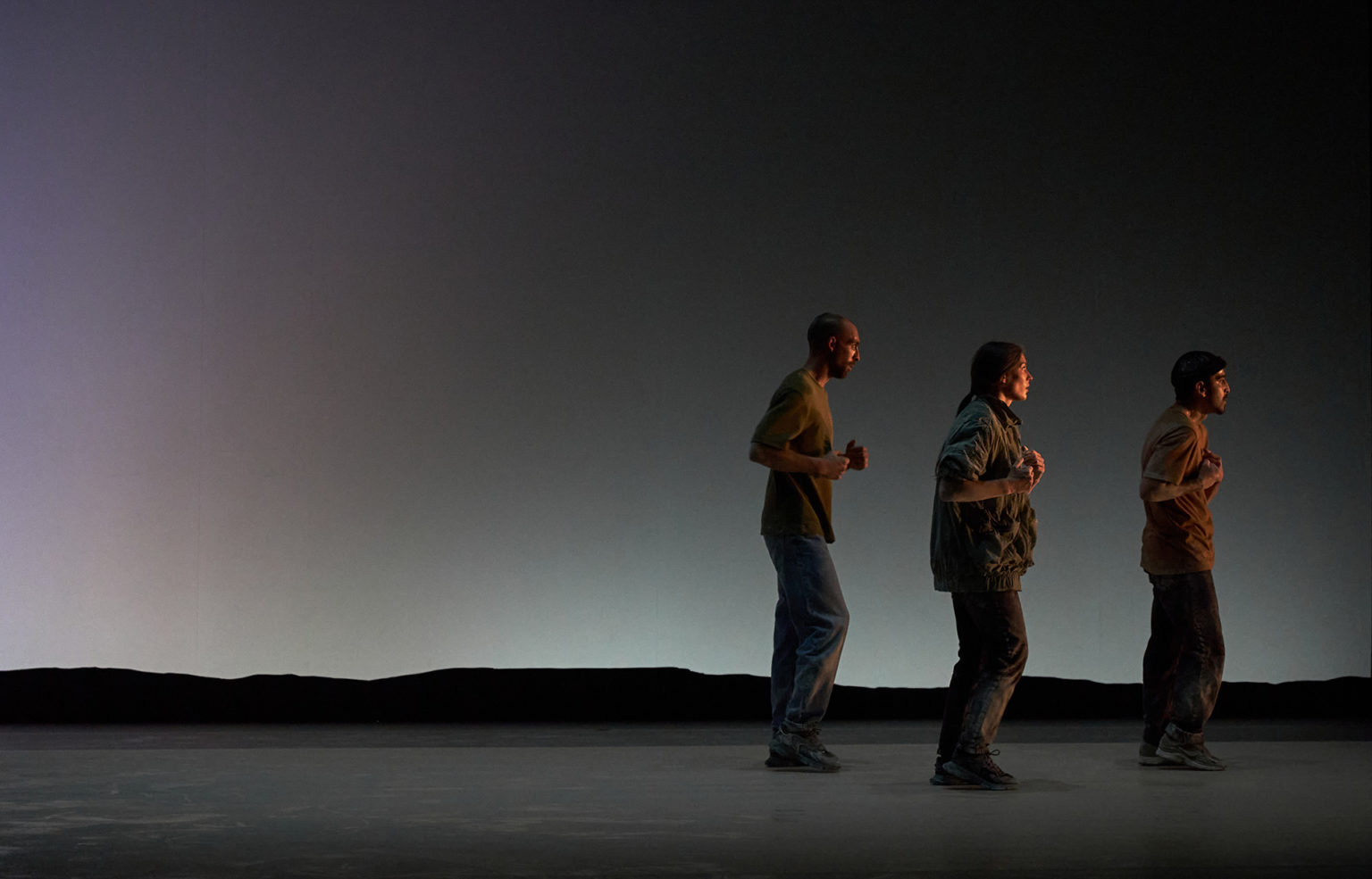 Photo du spectacle "Paysage" où l'on voit les 3 danseurs debout, les uns derreière les autres, comme s'ils couraient.
