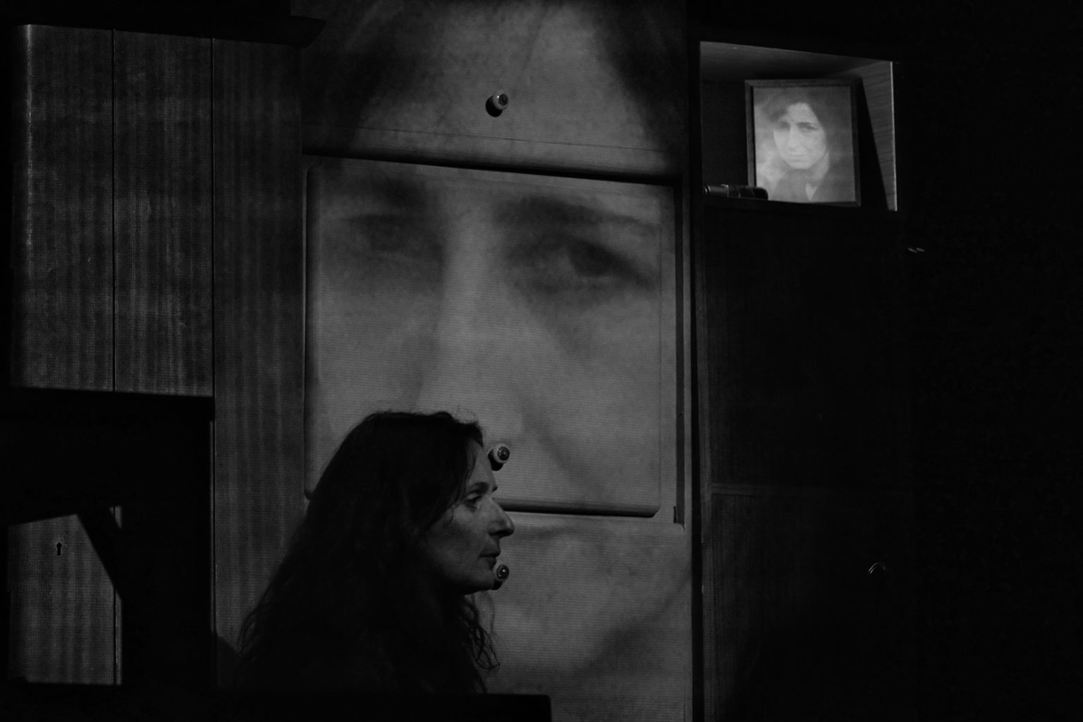Photo en noir en blanc où l'on voit Jasmina Douieb et derrière elle le visage de sa mère projeté sur le décor.