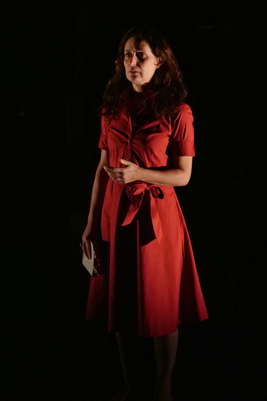 Jasmina Douieb est debout et porte une robe rouge. Elle tient un livre en mains.