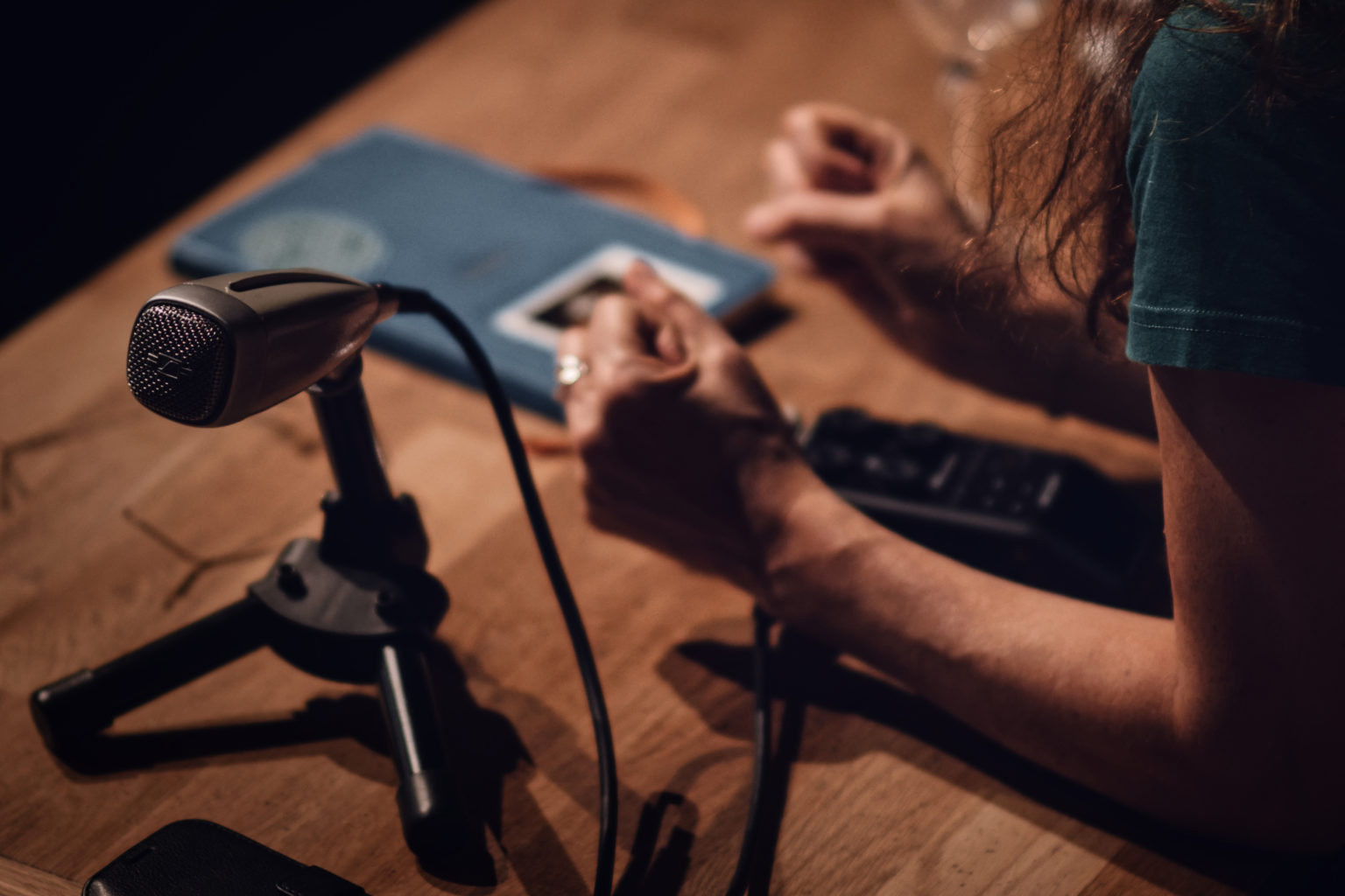 On voit les avant-bras de Jasmina Douieb appuyés sur une table en bois. Autour d'elle, un micro - type radio - et un enregistreur.