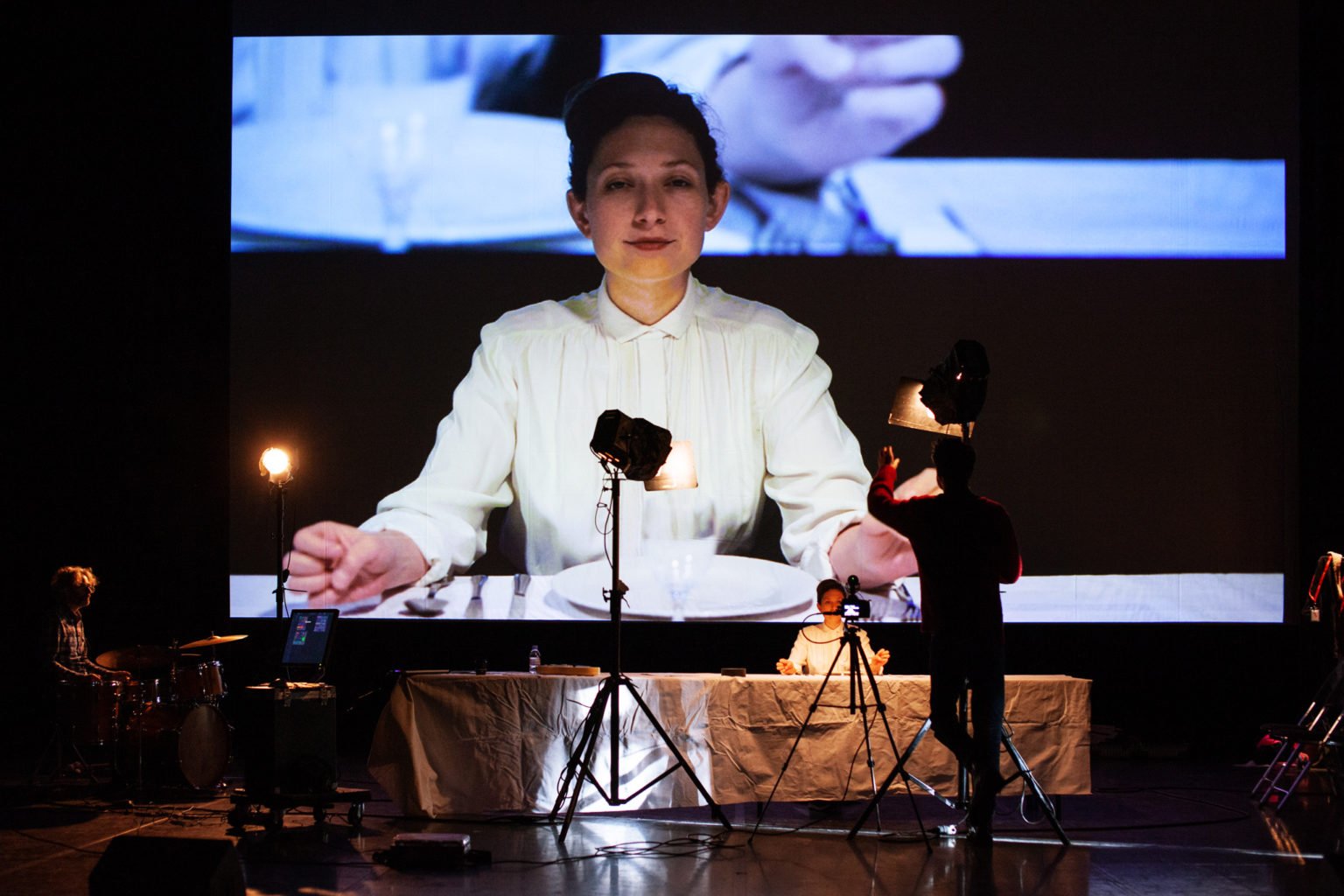 Ariane Loze est assise à une table, comme sur un plateau de cinéma. Un écran est derrière elle et projette son image.