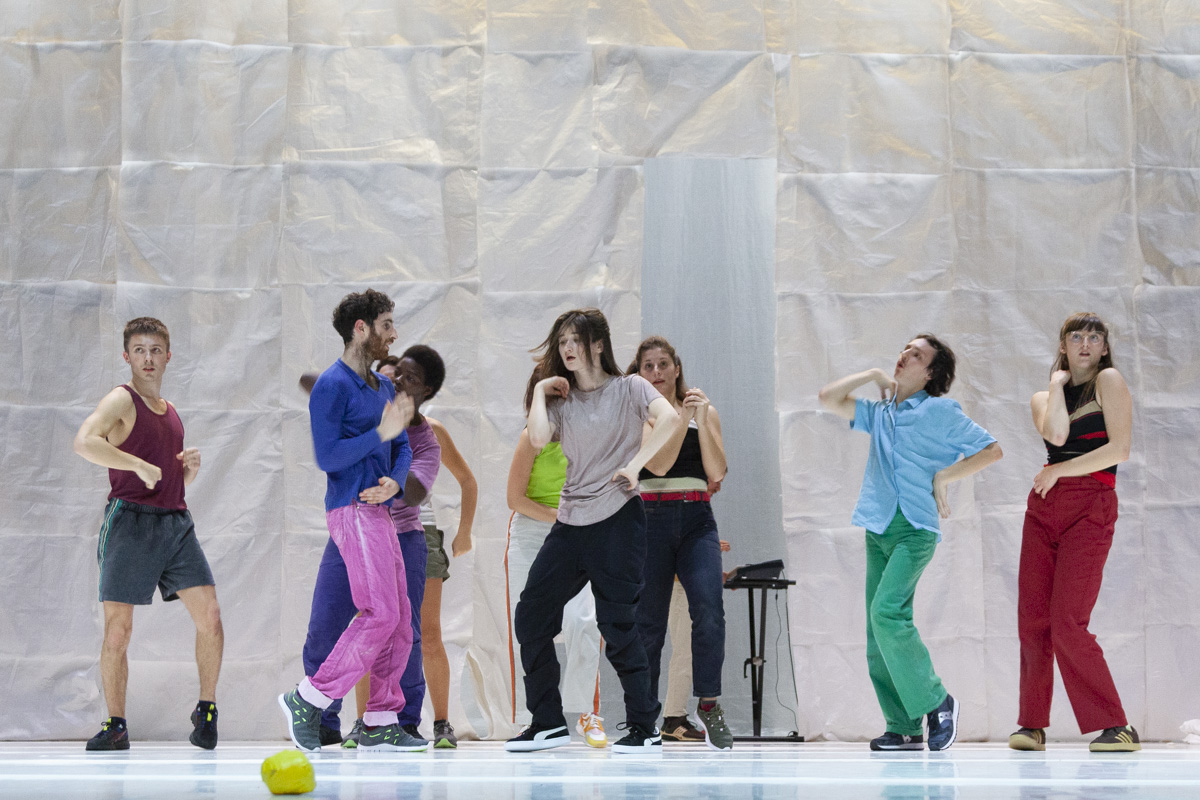 Sept personnes dansent sur une piste, cinq sont bien visibles sur la photo tandis que deux autres sont derrière. Ils sont tous habillés en couleurs.