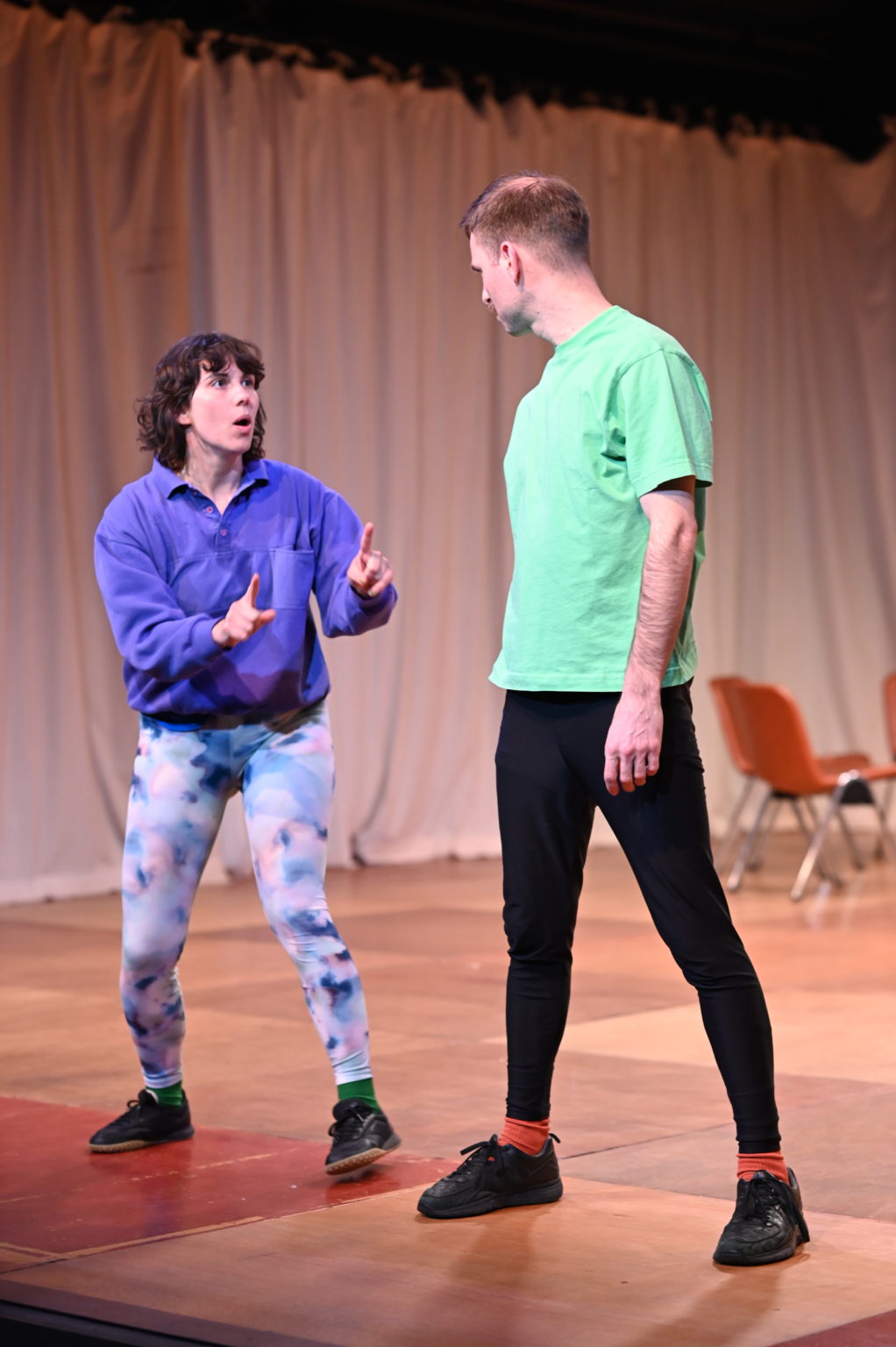 Les deux comédiens (Cédric Coomans et Chloé Larrère) sont debout l'un à côté de l'autre. Chloé (qui joue le rôle de Fani) explique quelque chose à Cédric (qui joue le rôle de Filip). Ils portent des leggings de sport.