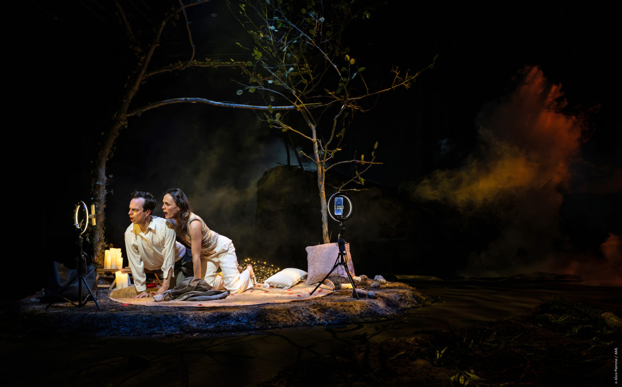 Un couple, joué par Aurelio Mergola et Sophie Leso, regardent tous les deux l'un de leurs téléphones, tels des influenceurs en plein direct. Ils ont recréé un petit cocon avec des bougies, des lampiottes dans un bout de forêt qui parait hostile.