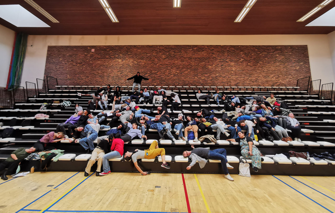 Des élèves participant au projet Pass à l'Acte font semblant de se reposer sur les gradins d'une salle de sport.