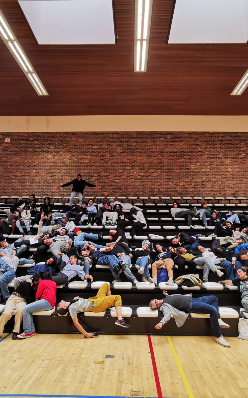 Des élèves participant au projet Pass à l'Acte font semblant de se reposer sur les gradins d'une salle de sport.