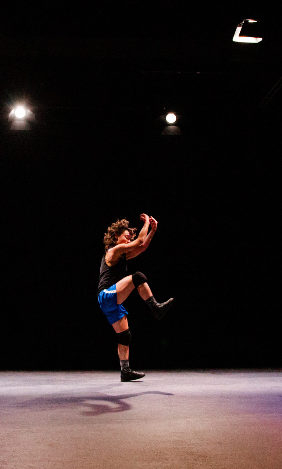 Une danseuse, en short, t-shirt et jambières, seule au milieu d'un plateau nu, danse et saute.