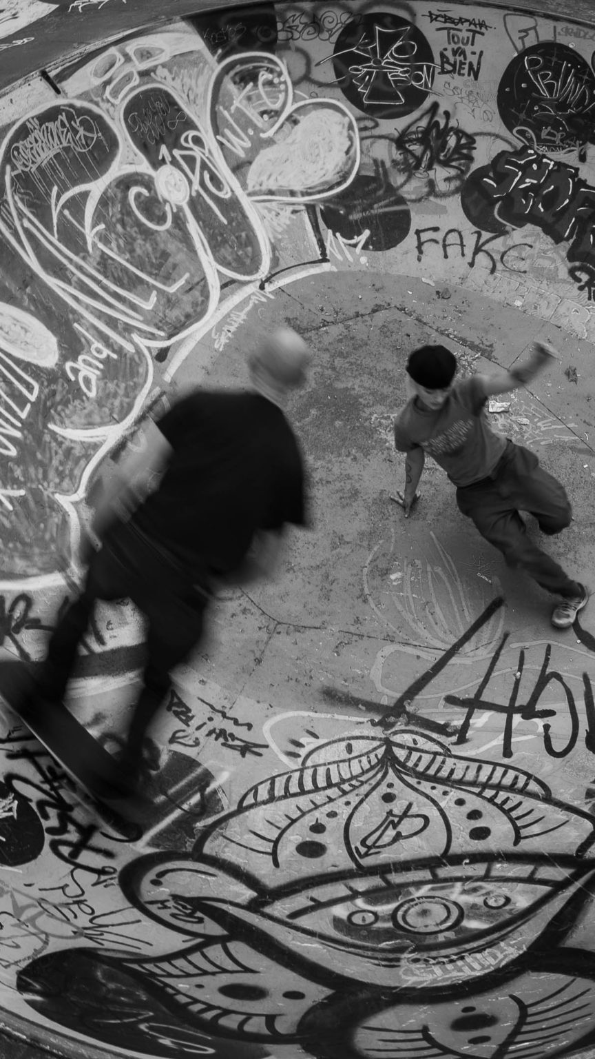 Dans un skatepark, un jeune homme fait du skate et un autre du breakdance.