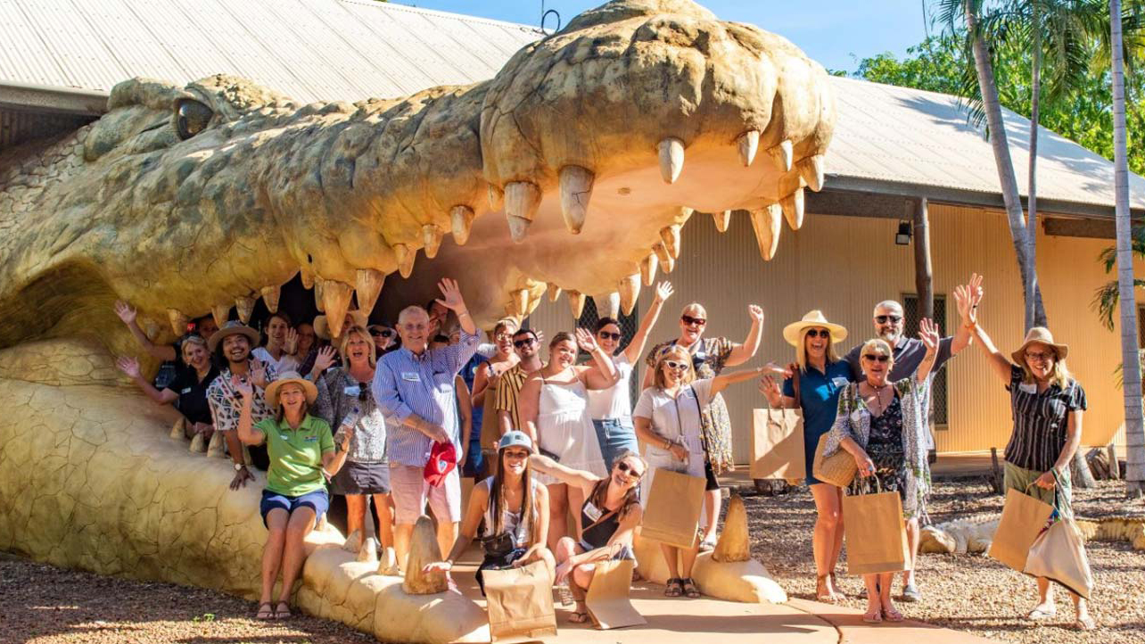 Un groupe de personnes posent devant la caméra avec les bras levés. Ils sont dans la bouche d'un grand crocodile.