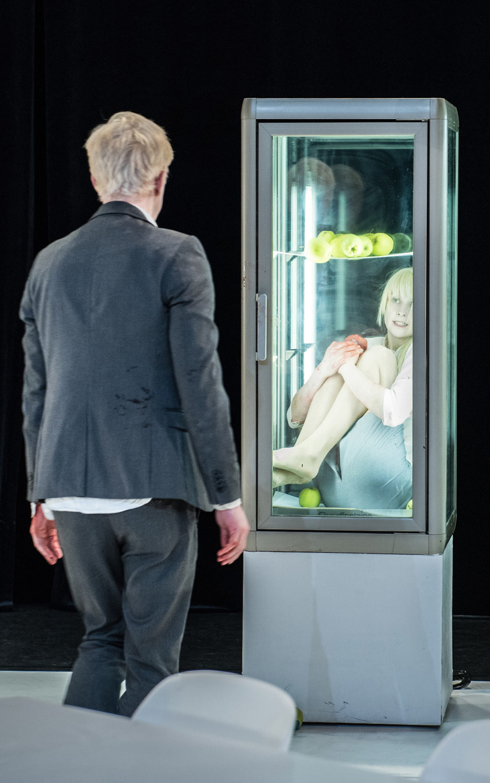 La comédienne Sophie Linsmaux est recroquevillée dans un frigo vertical. Elle regarde vers le comédien Aurelio Mergola qui nous tourne le dos et s'avance vers elle. Il a du sang sur elle, et elle aussi. Ils portent tous les deux des tailleurs.