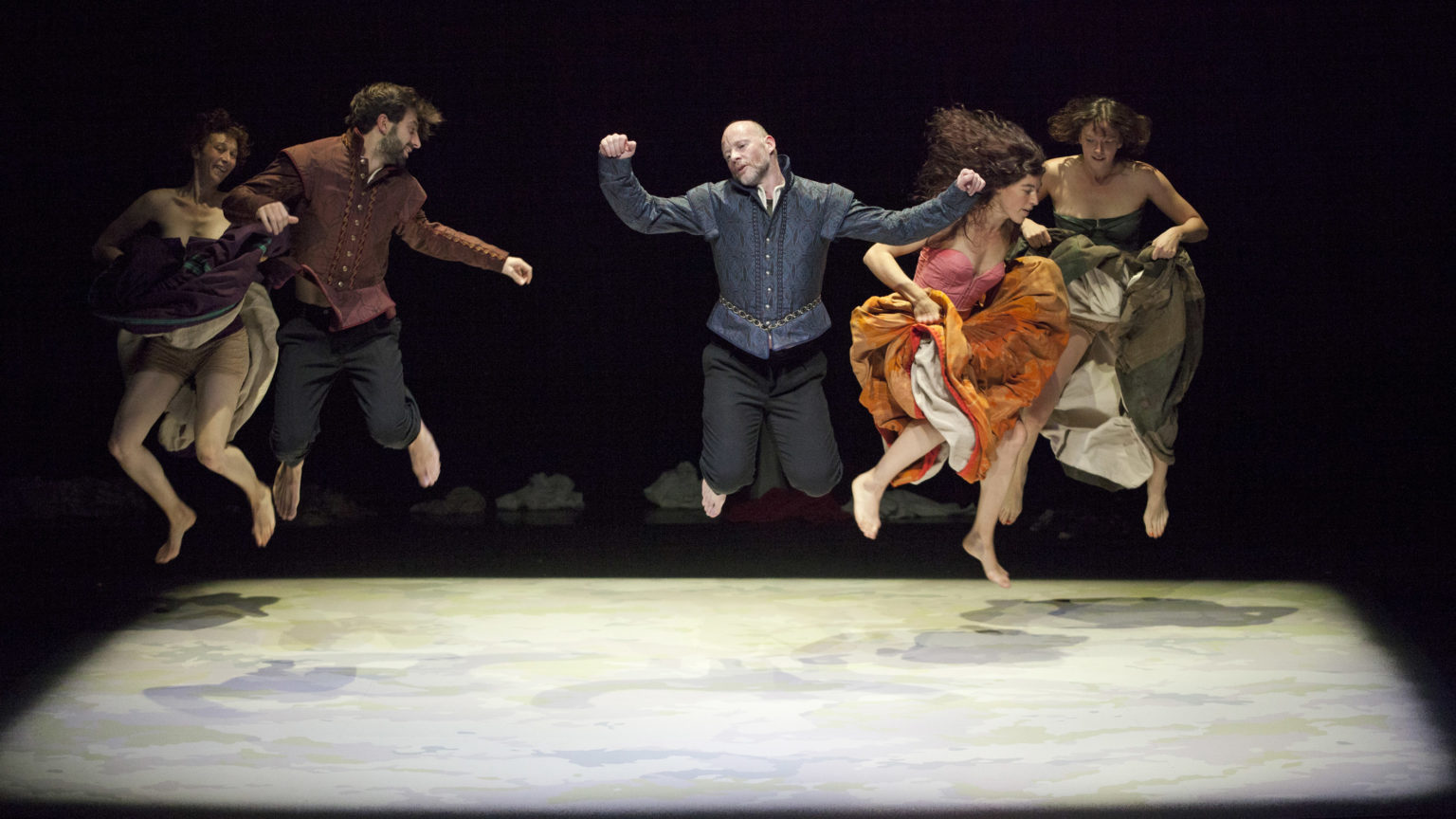 Un groupe de danseurs·euses costumés sautent en l'air sur scène.