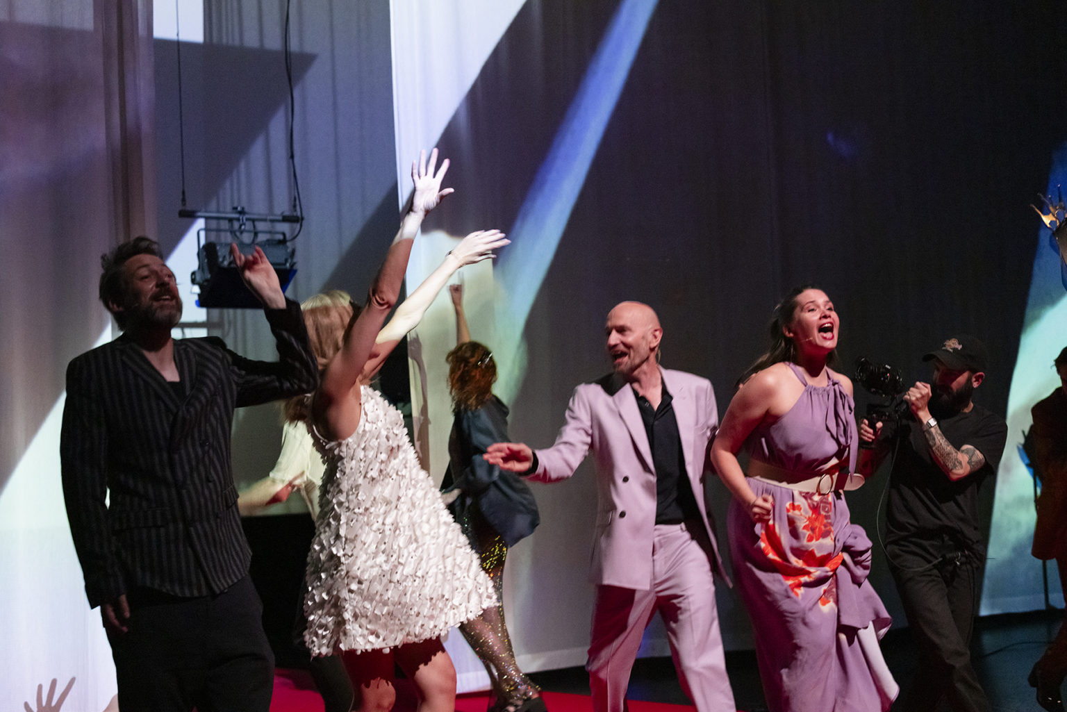 Les acteurs et actrices habillées en vêtements de soirée ont l'air heureux, crient, lèvent les bras.