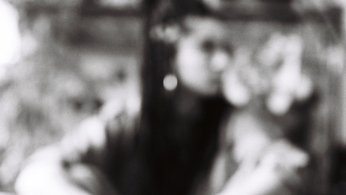 Yasmine Yahiatène est assise, les mains sur les genoux. Elle regarde sur le côté. La photo est floue et en noir et blanc.