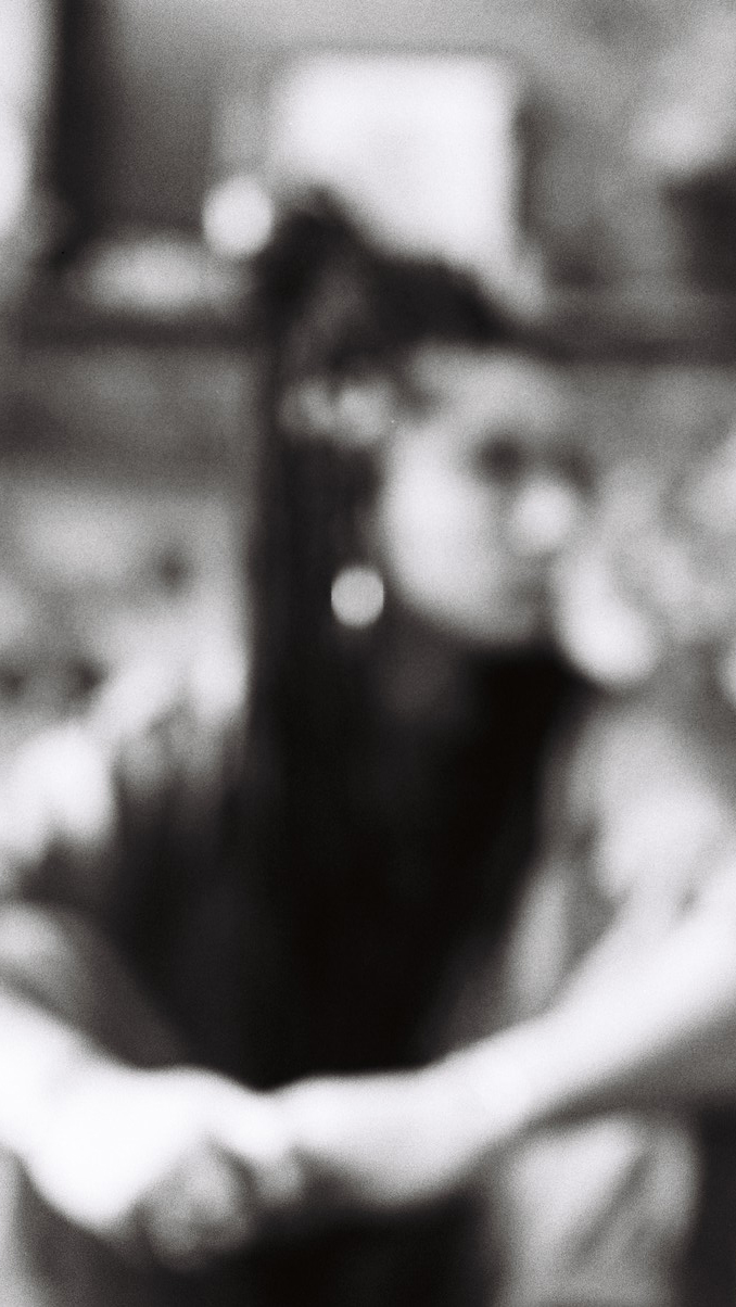 Yasmine Yahiatène est assise, les mains sur les genoux. Elle regarde sur le côté. La photo est floue et en noir et blanc.