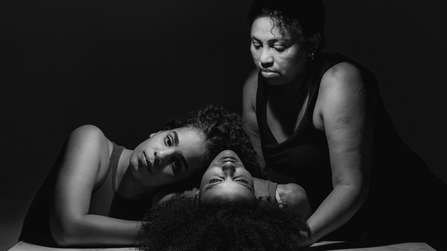 Photo en noir et blanc représentant 3 femmes, 3 travailleuses migrantes habitant au Liban, devant une table en marbre. Leurs visages s'y reflètent.