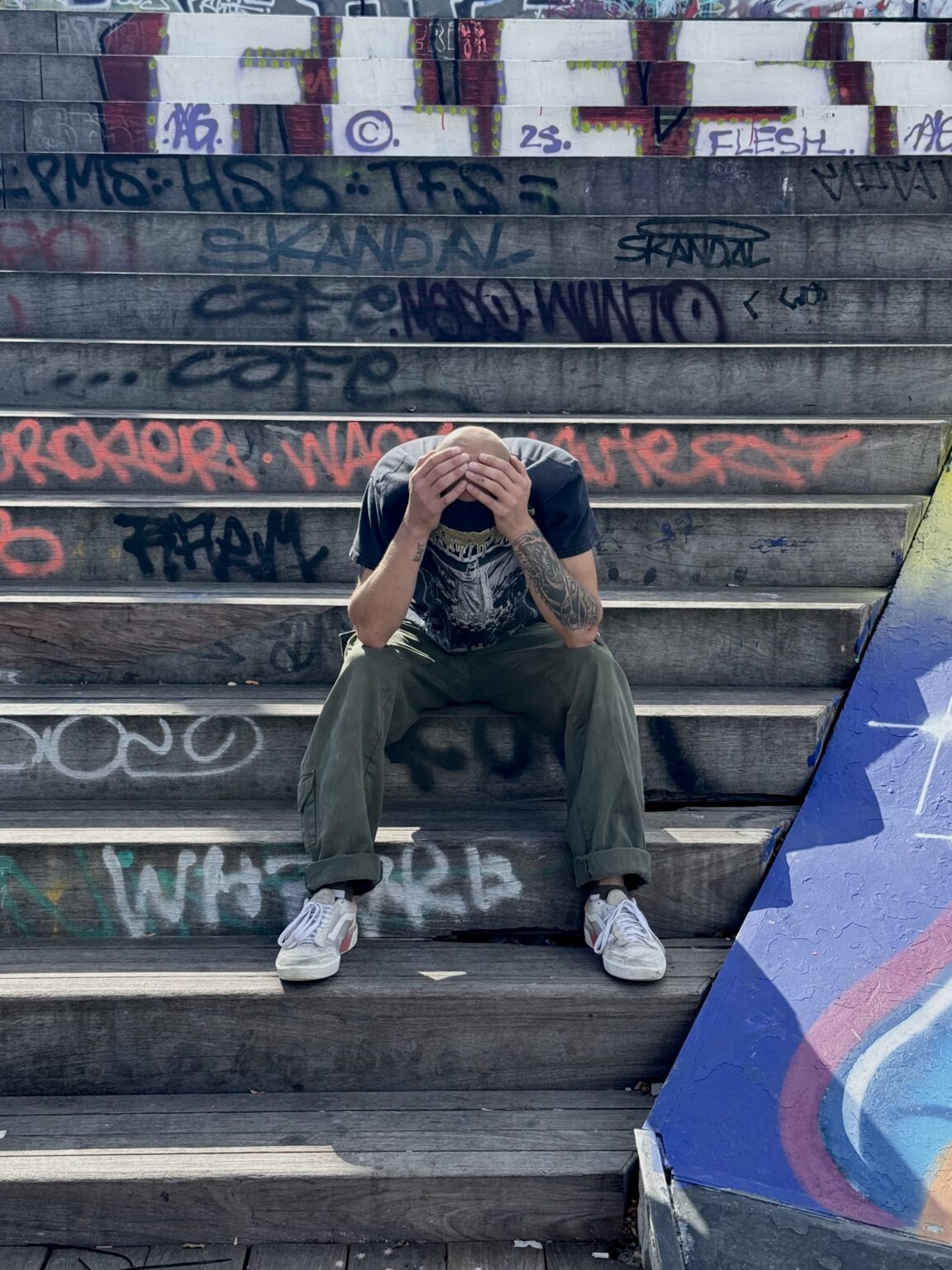 Un garçon (danseur ou skateur) est assis sur les marches derrière le skatepark et se tient la tête dans les mains.
