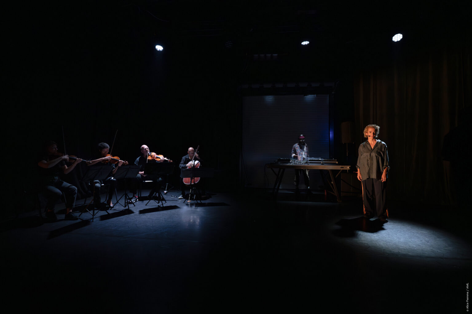 Stéphanie Blanchoud est debout, dans la pénombre, tout à droite. Au milieu, le DJ et à gauche le quatuor à cordes.