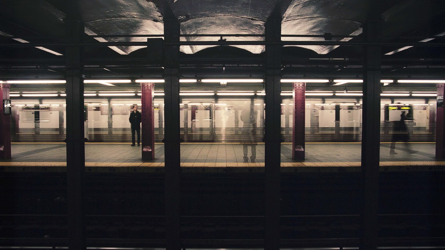 Des personnes sont debout sur un quai de métro (type new-yorkais).