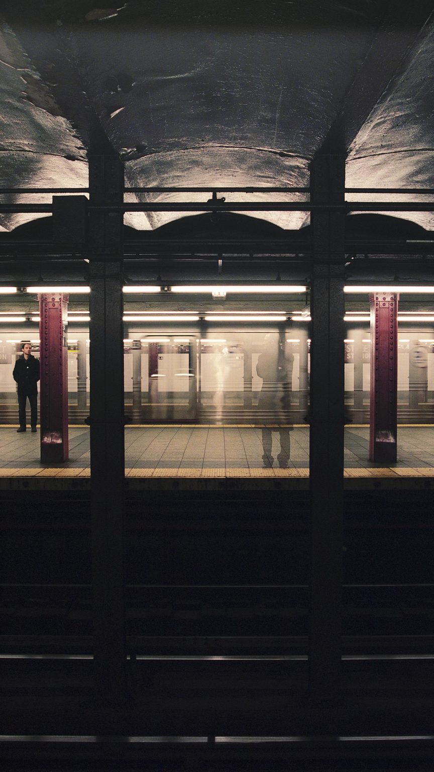Des personnes sont debout sur un quai de métro (type new-yorkais).