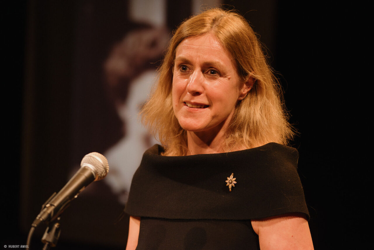 Geneviève Damas se tient debout derrière un micro.