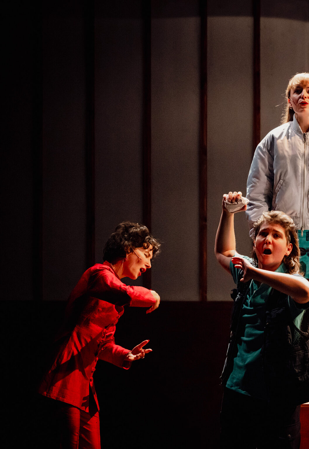 Sur une petite estrade, la chorale composée de cinq chanteurs répète. Ils prennent tous des poses étranges, type statues. Derrière eux, il y a un grand paravent en bois. Sur la gauche, la cheffe de choeur chante avec eux, à fond dedans.