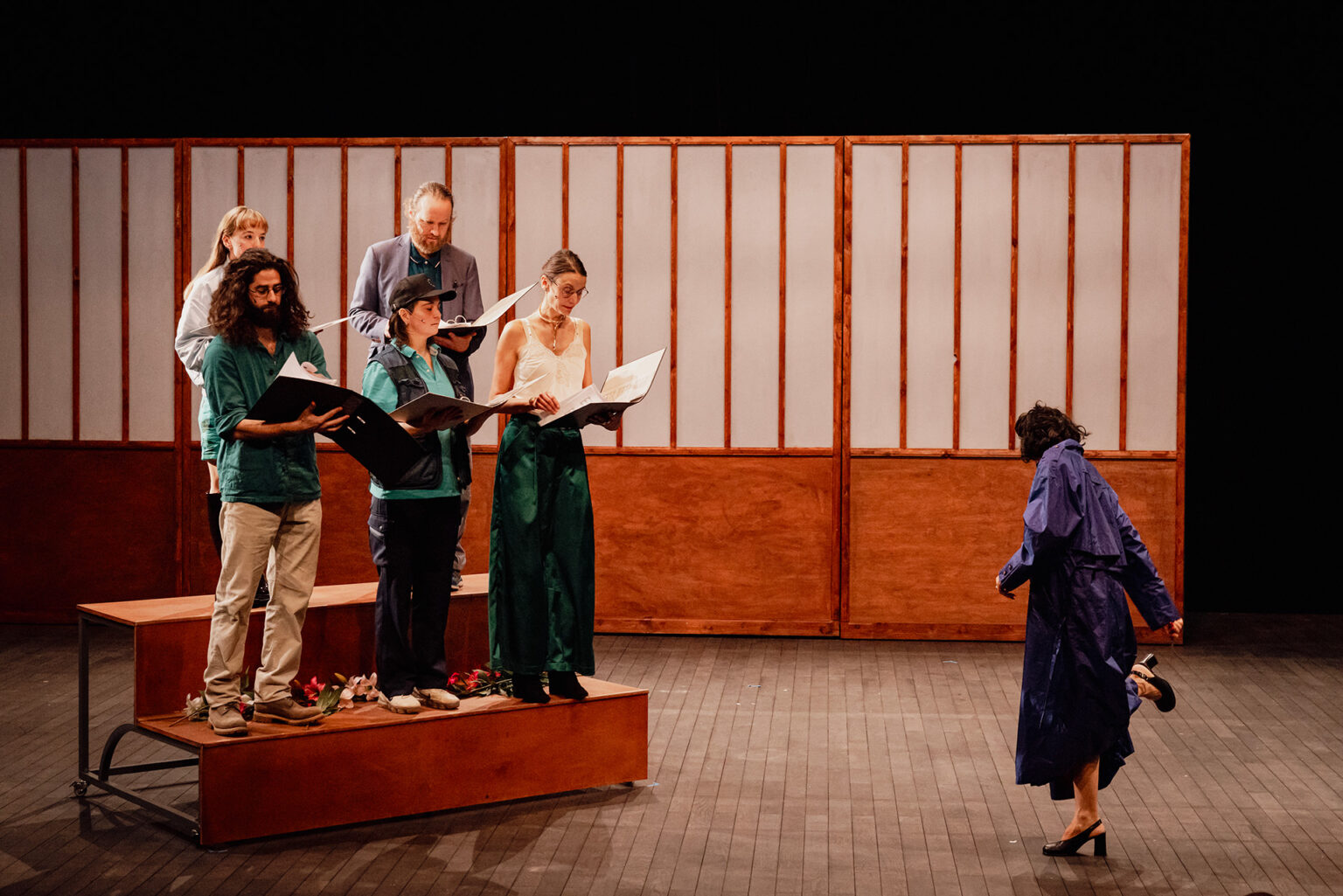 Sur un petit strapontin, la chorale composée de six chanteurs répète. Derrière eux, un grand paravent. Sur la droite, la cheffe de choeur semble plus intéresser par ses chaussures que par eux.