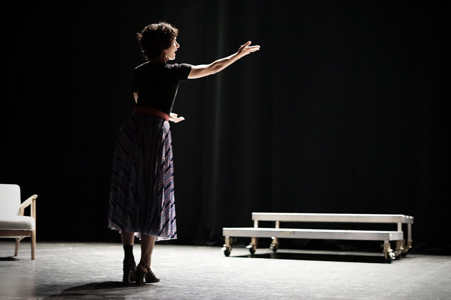 La cheffe de choeur est de 3/4, debout, une main tendue en avant.