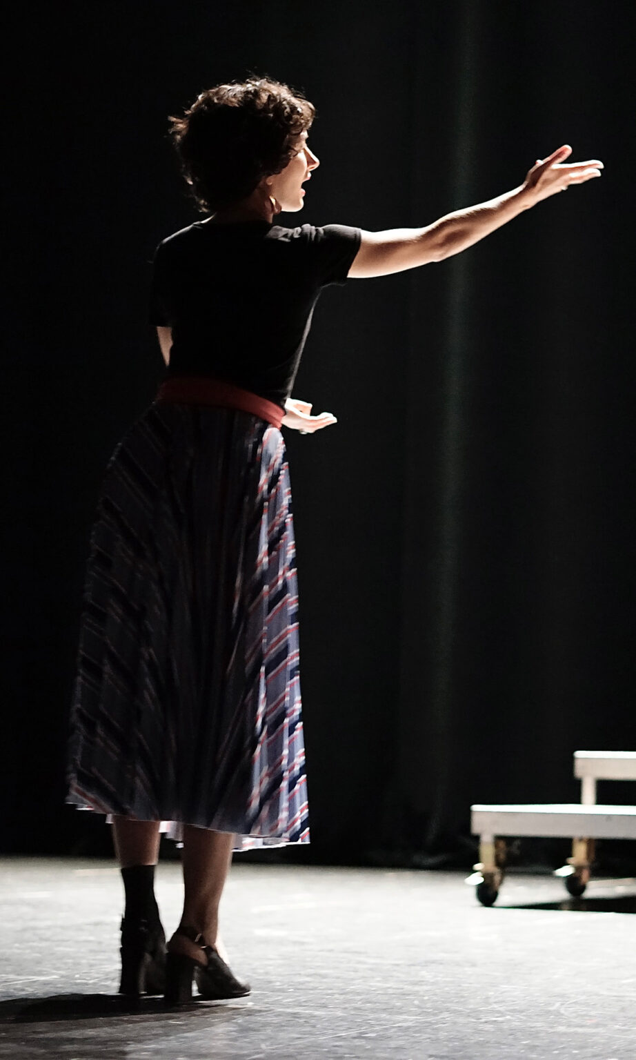 La cheffe de choeur est de 3/4, debout, une main tendue en avant.