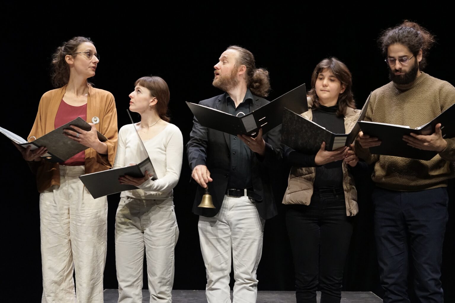 Les participants de la chorale les uns à côté des autres. Deux d'entre eux ont l'air de discuter. Ils portent tous leur partition en mains.