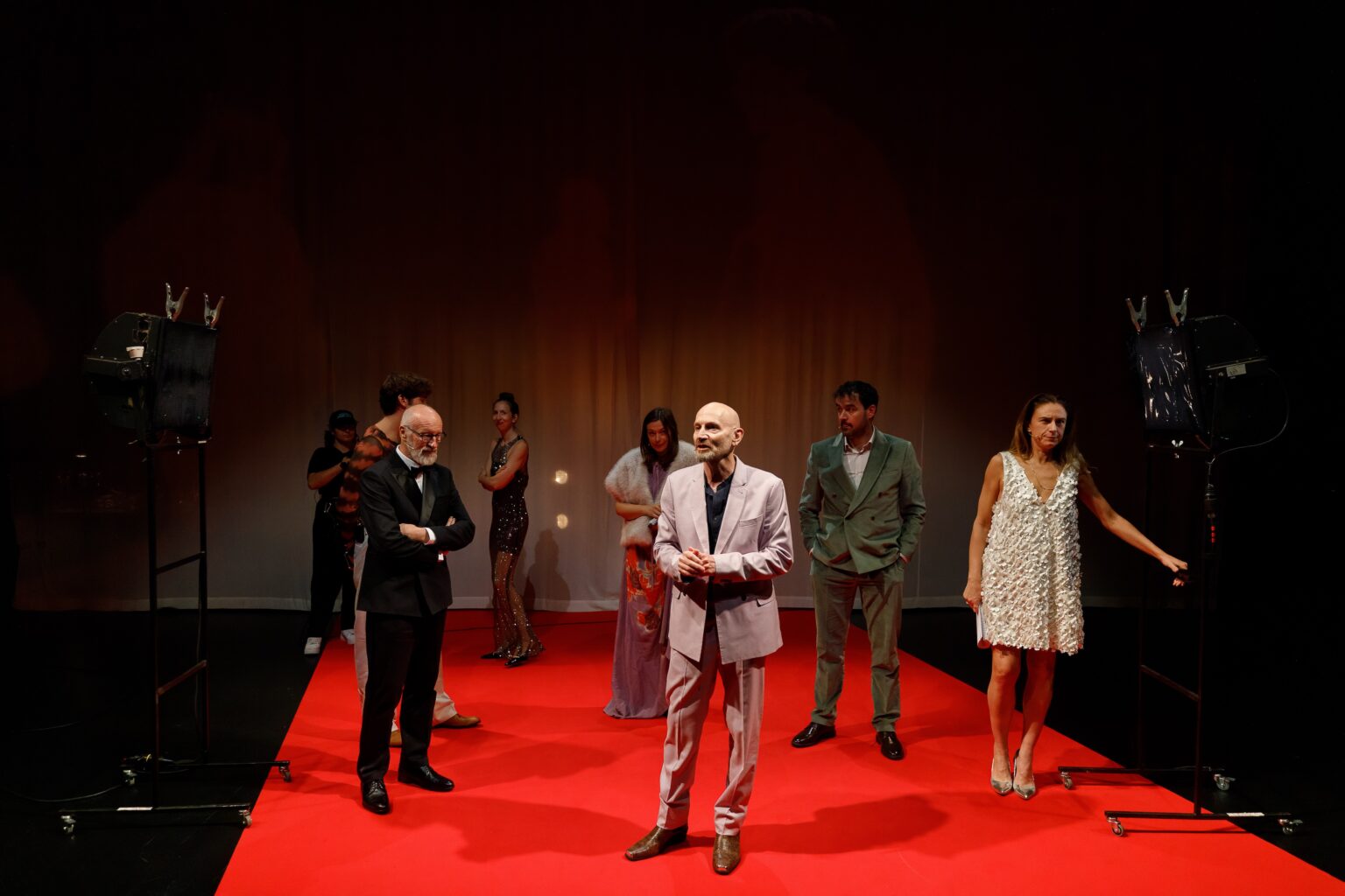Sur un tapis rouge, les acteurs et actrices sont debout, habillés avec des vêtements chics. Ils prennent tous et toutes l'espace du tapis rouge.