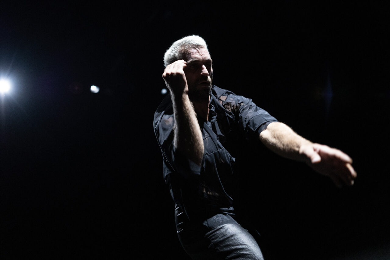 Micaël Florentz est courbé, la main droite relevée à hauteur de son visage. Il porte des vêtements sombres.