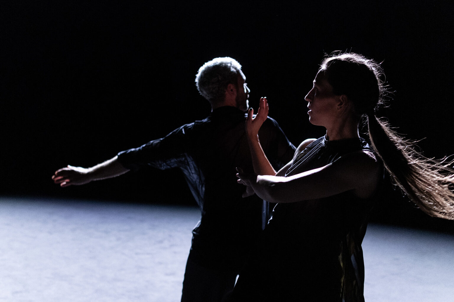 Angela Rabaglio et Micaël Florentz dansent l'un à côté de l'autre, en habits foncés. Le tapis de danse est clair. Il lui tourne le dos. Elle est de profil et lève une main vers son visage.