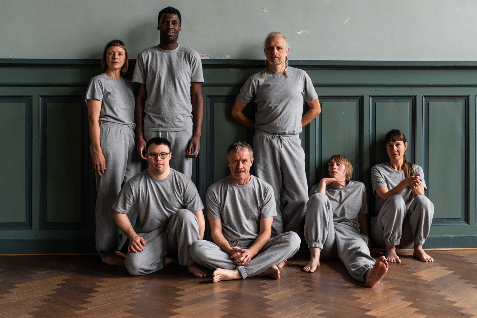 Photo de groupe des 6 danseurs. Ils sont tous habillés en gris. Trois sont debout, 4 sont assis. Ils posent pour la photo et regardent l'objectif.