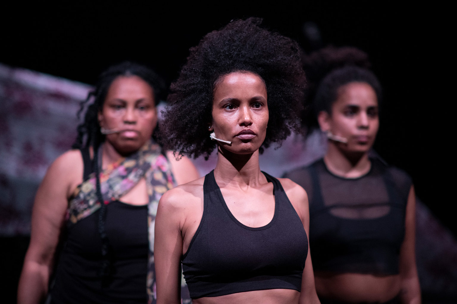 Les trois interprètes sont debout, les bras le long du corps, les unes à côté des autres. Elles regardent droit devant elles.