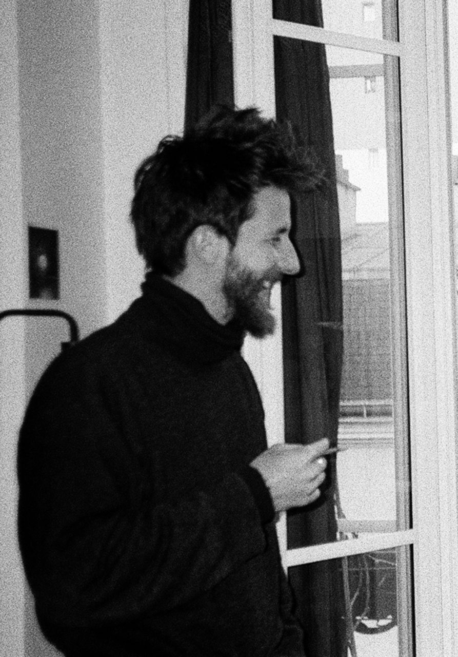 Portrait en noir et blanc de Gabriel Sparti. Il est de profil, sourit et porte un pull.