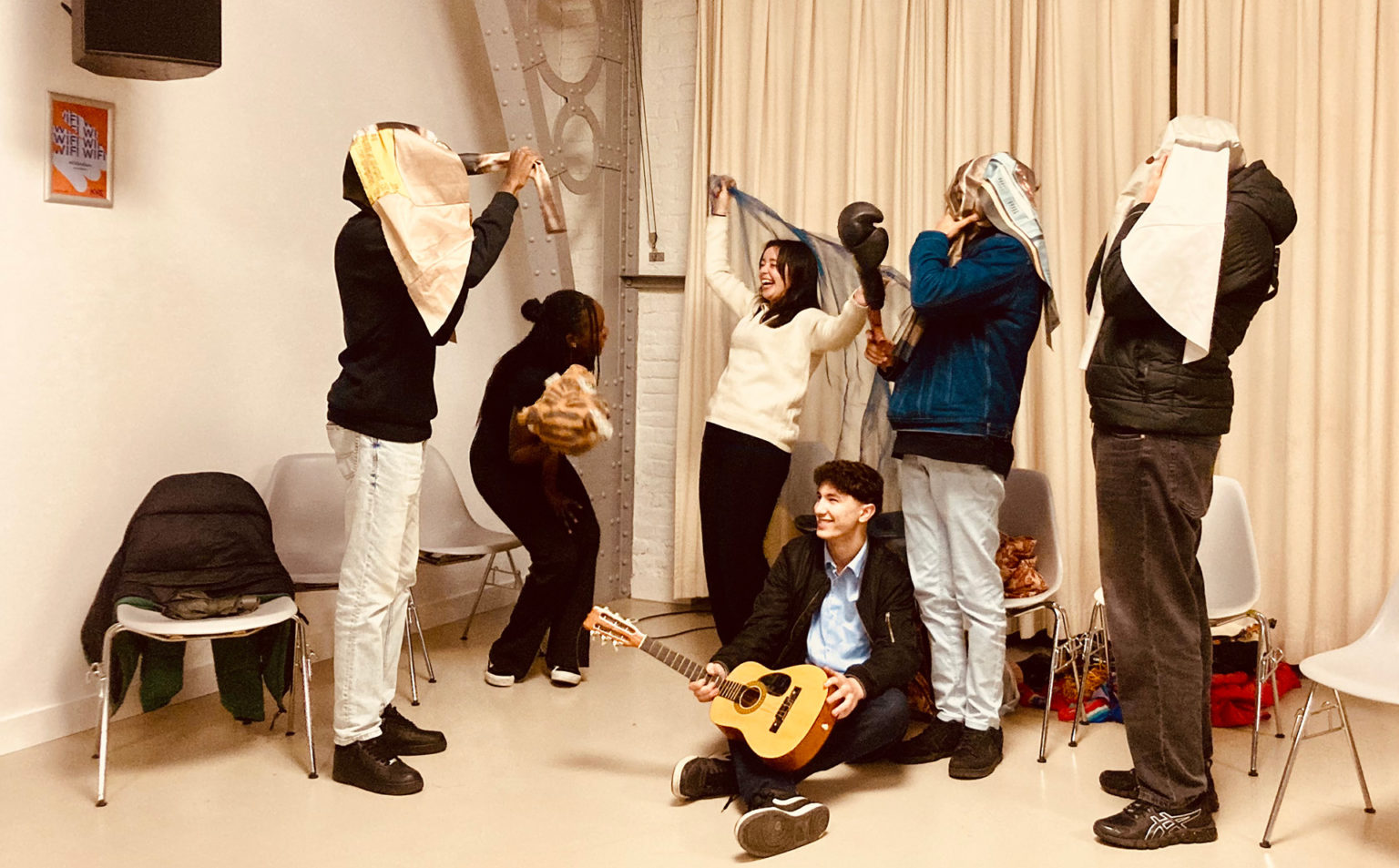 Atelier avec le Pass à l'Acte. Cinq jeunes sont debout, rient et portent des accessoires. L'un d'entre eux est par terre avec une guitare entre les mains
