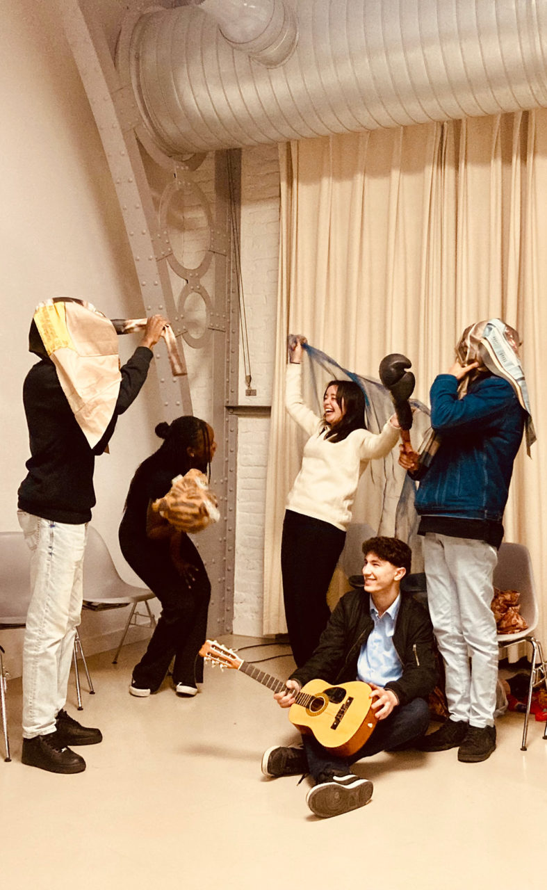 Atelier avec le Pass à l'Acte. Cinq jeunes sont debout, rient et portent des accessoires. L'un d'entre eux est par terre avec une guitare entre les mains