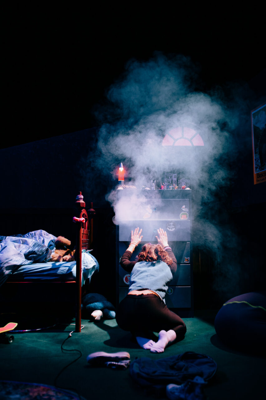 Une actrice est de dos, sur les genoux. Elle essaie de refermer un tiroir d'une commode de laquelle sort de la fumée. Elle est dans une chambre, un lit est à côté d'elle. Des objets de toutes sortes trônent sur le meuble.